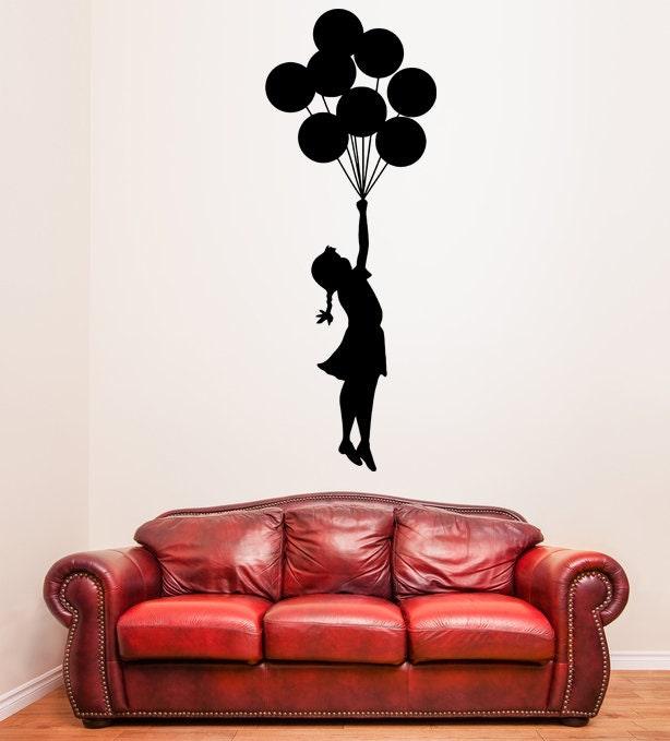 Banksy Girl With Balloons wall decal above a red couch, showcasing iconic street art vinyl sticker for home decor.