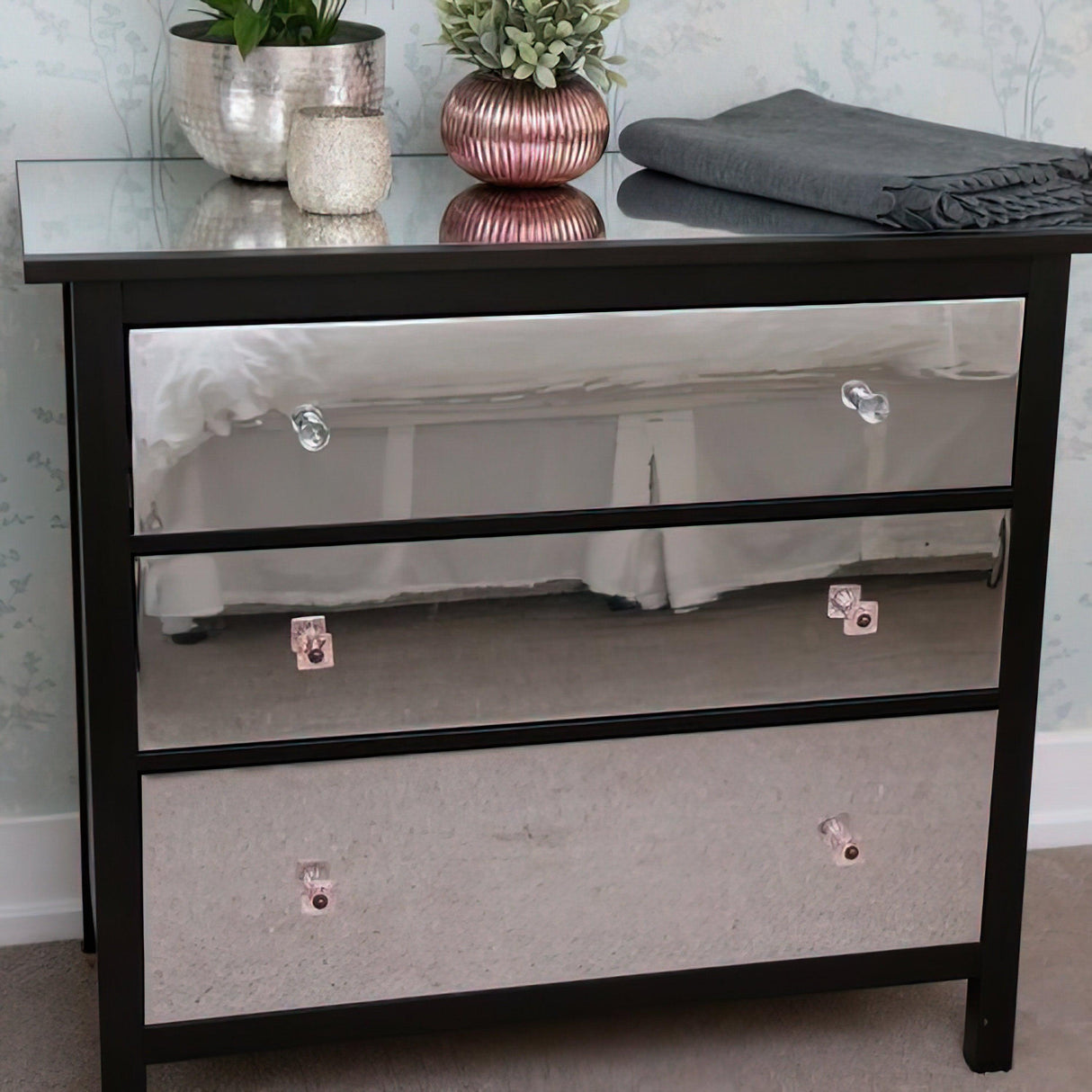 Stylish black dresser with mirrored drawers, potted plants, and a folded blanket on top.
