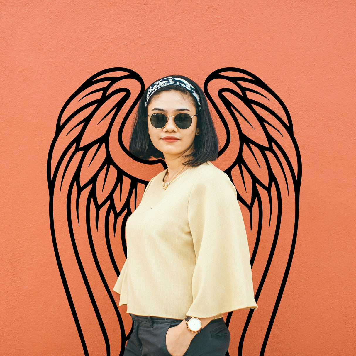 Woman wearing sunglasses standing against a wall with angel wings vinyl decal, showcasing stylish wall decor.