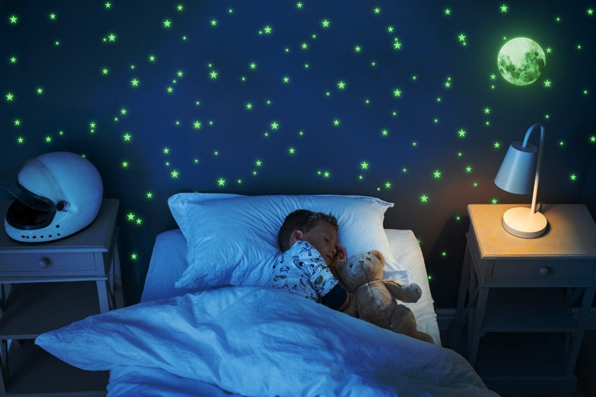 Child sleeping peacefully under glow in the dark stars and moon wall decals in a cozy bedroom.