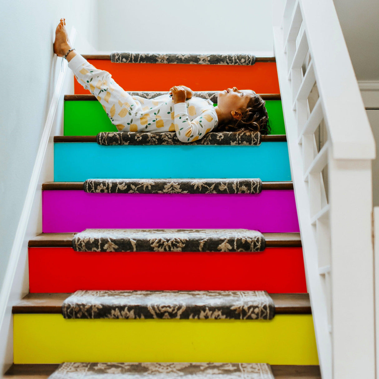 Child relaxing on rainbow-colored stair riser stickers, adding a playful touch to the staircase decor.