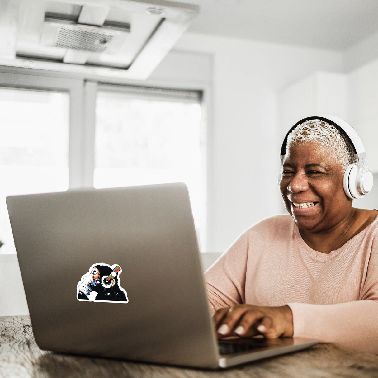 Happy older woman with headphones using a laptop featuring a glowing music monkey decal, enjoying her time.