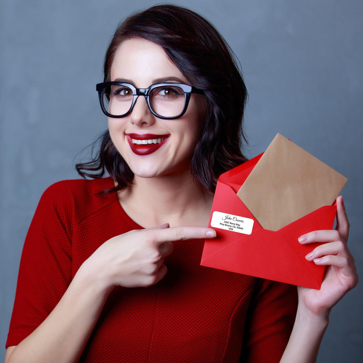 Woman with glasses holding a red envelope featuring a custom clear address label for personalized mailing.