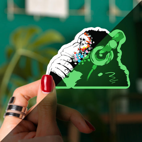 Glow in the dark monkey vinyl sticker held in hand, featuring playful design with headphones and vibrant colors.