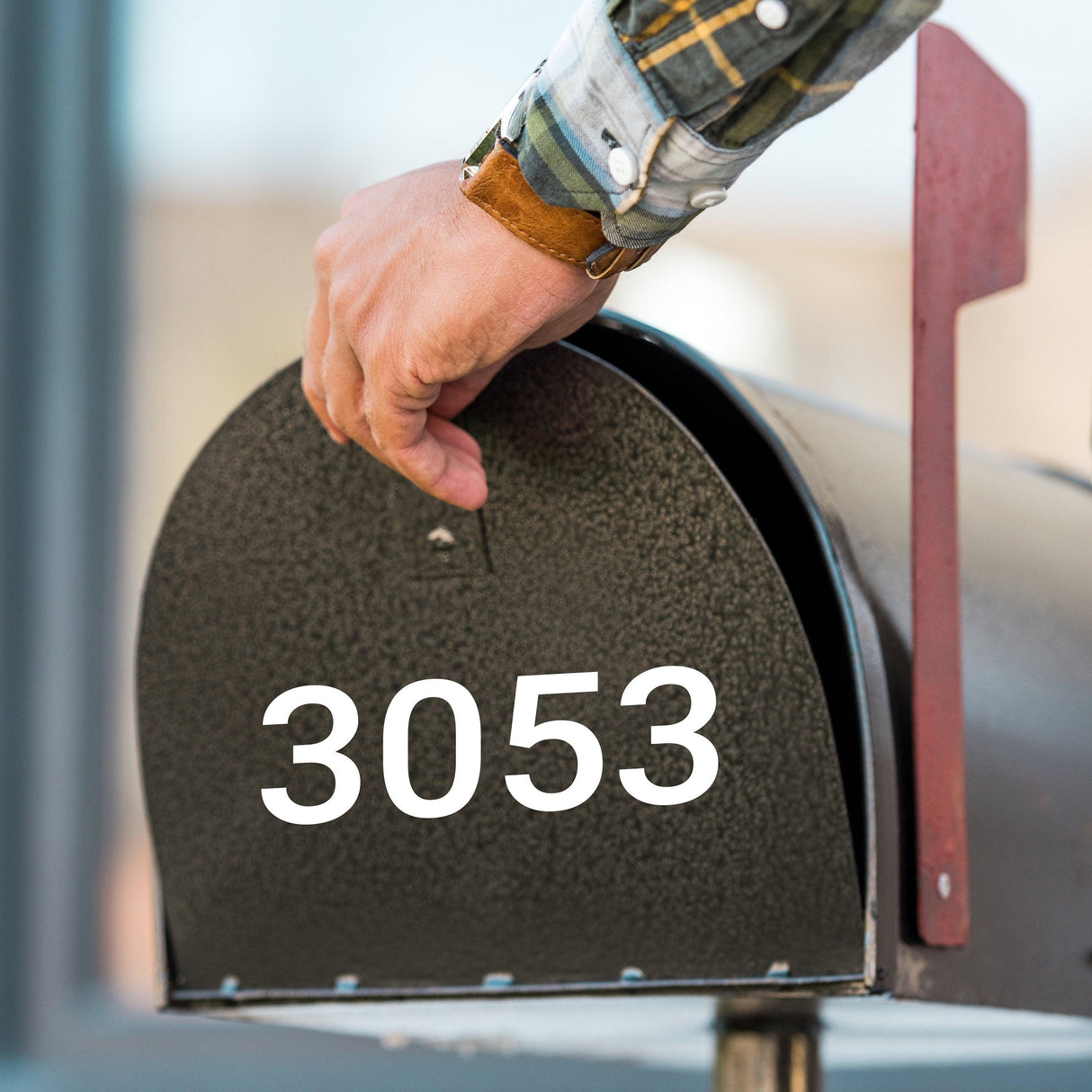 Hand placing a mail into a black mailbox with the number 3053 for personalized address display.