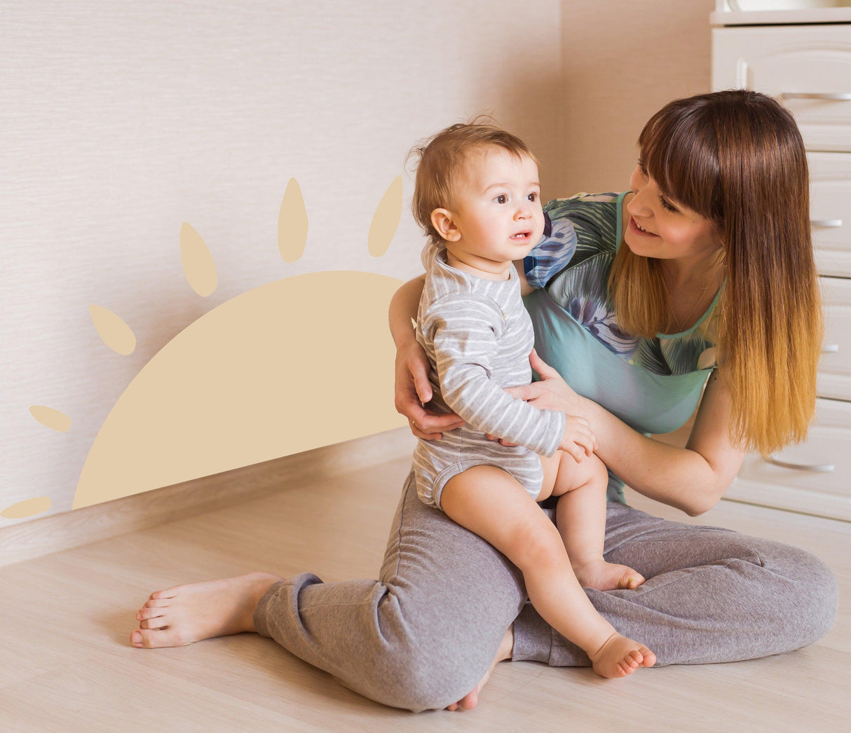 Woman and child sitting on the floor with a cheerful sun wall decal in a cozy interior space.