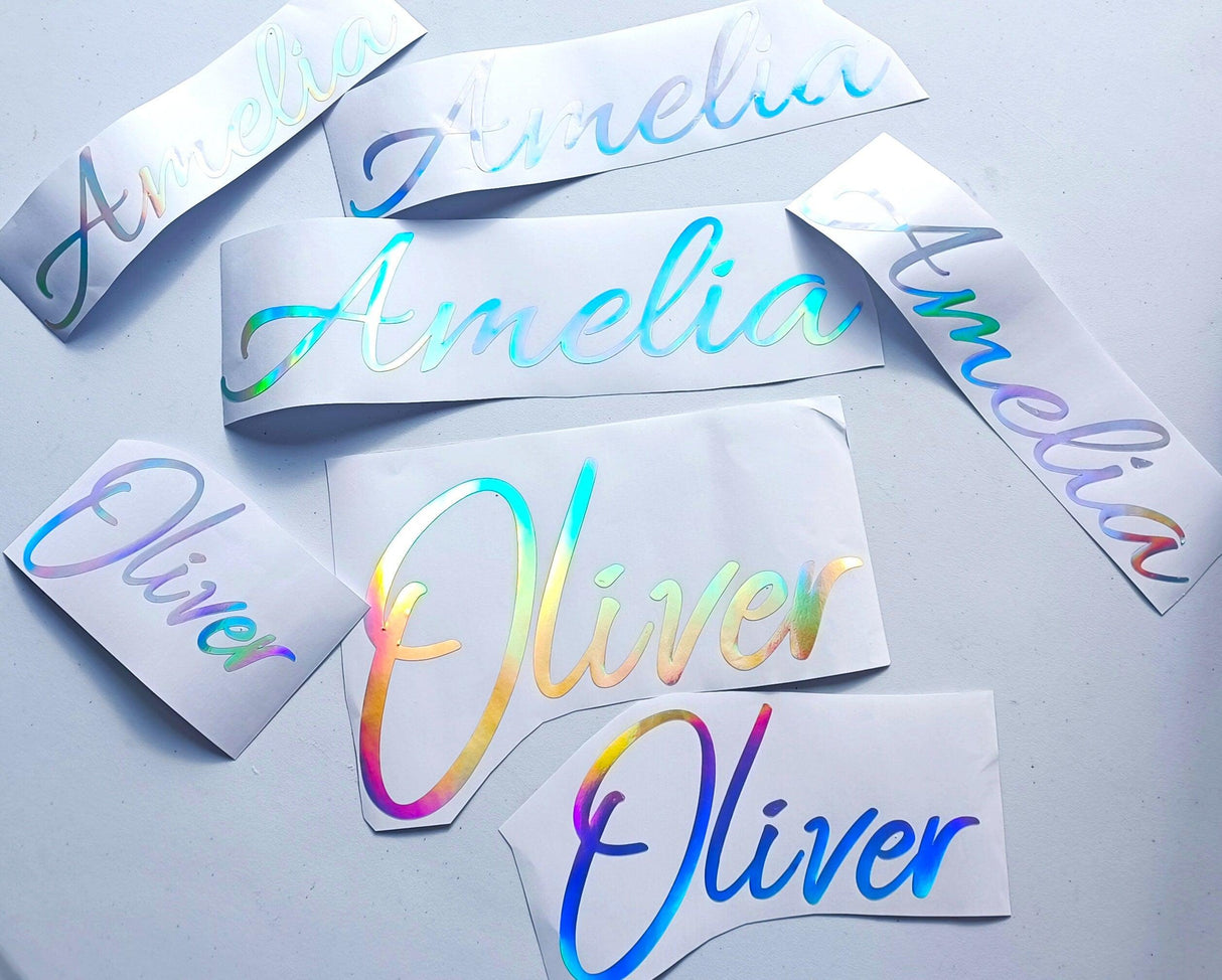 Personalized vinyl name decals featuring 'Amelia' and 'Oliver' in rainbow holographic finish.