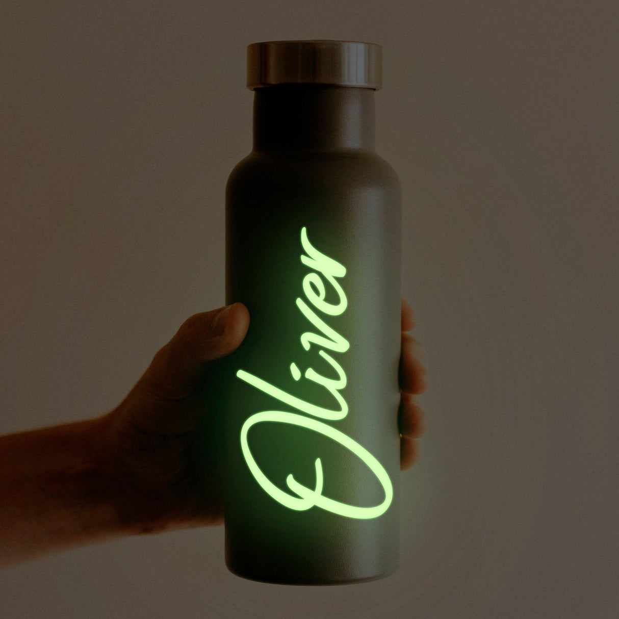 Personalized glow in the dark name decal on a dark water bottle held in hand, featuring the name 'Oliver'.