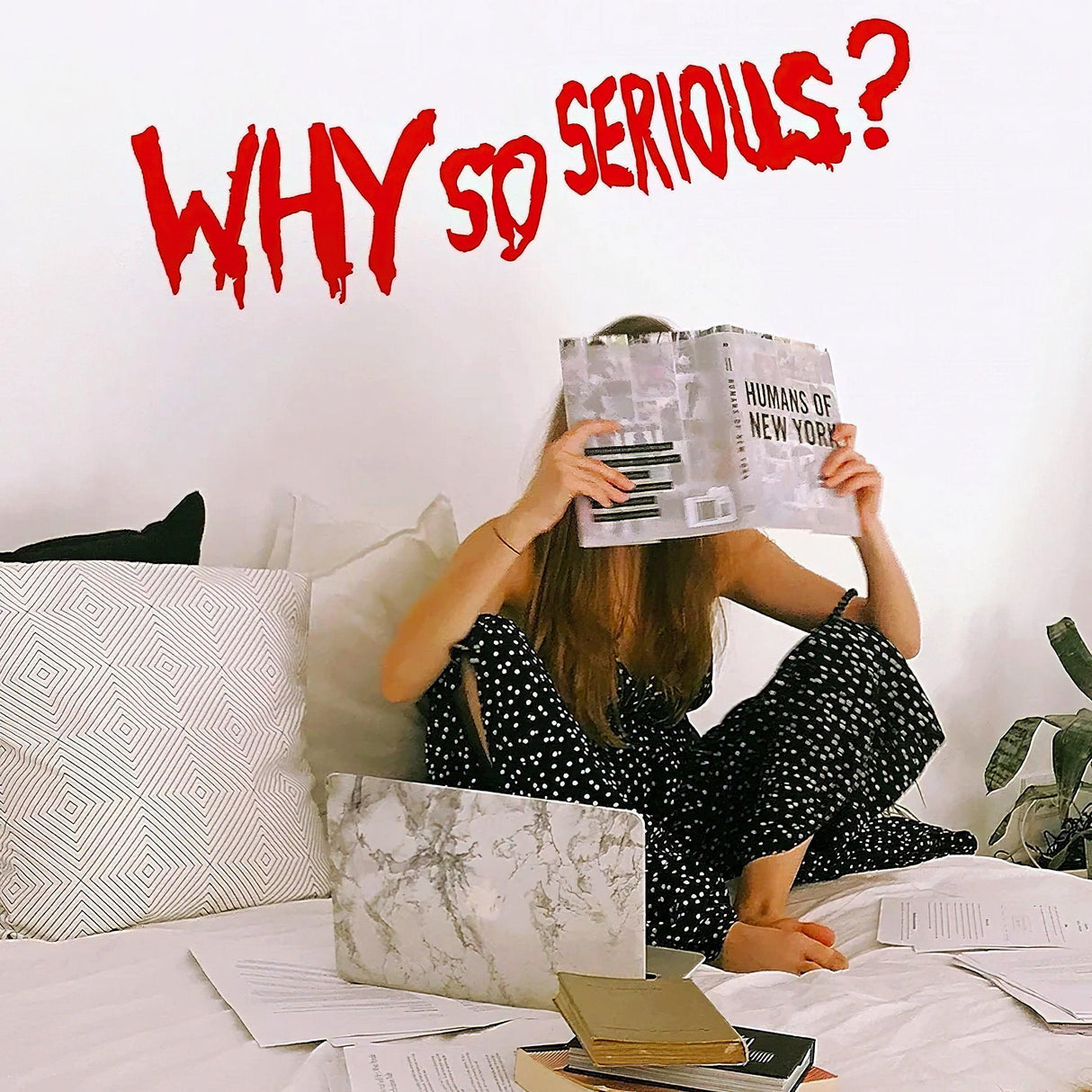 Young woman reading a magazine with 'Why So Serious?' vinyl sticker on the wall above her in a cozy setting.