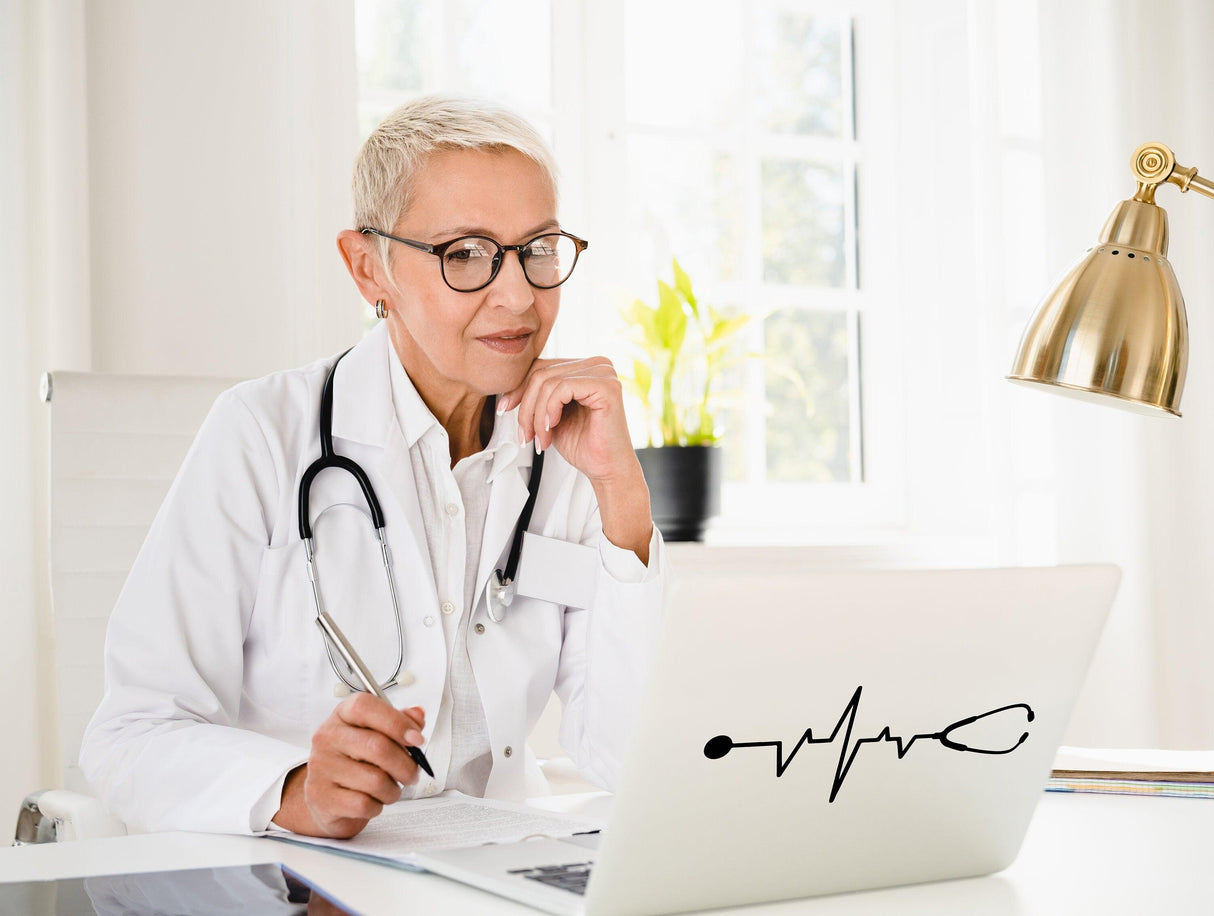 Doctor working on a laptop with a stethoscope and heartbeat decal in a bright office setting.