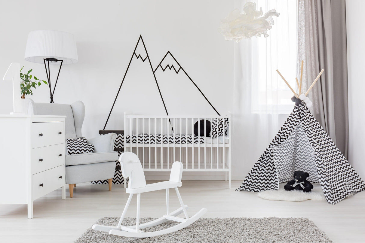 Stylish nursery featuring black mountain wall decals, modern crib, and playful tent decor, creating a cozy atmosphere.