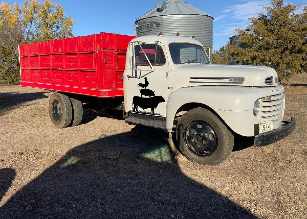Vintage farm truck with red cargo bed and farm animal decals parked in rural setting.