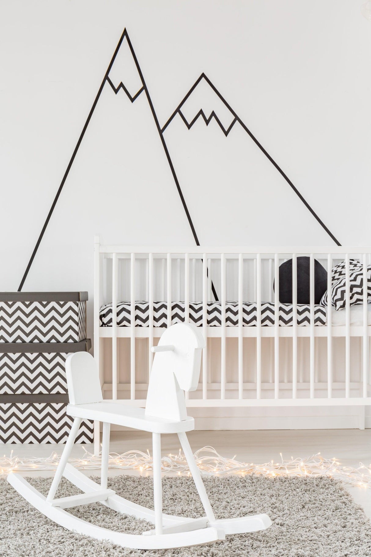 Modern nursery featuring black mountain wall decals, a white rocking chair, and stylish bedding.