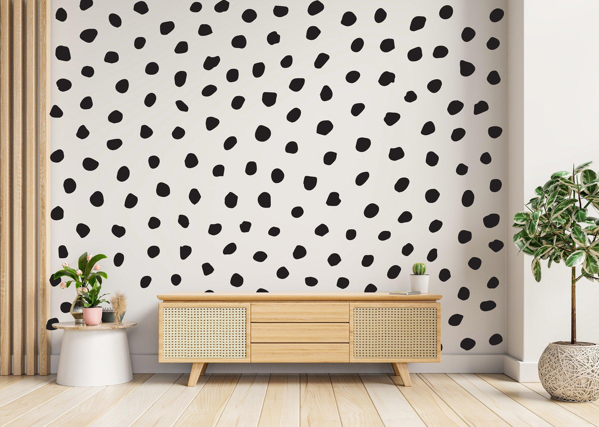 Modern black polka dots wall decal on white wall above wooden sideboard with indoor plant.