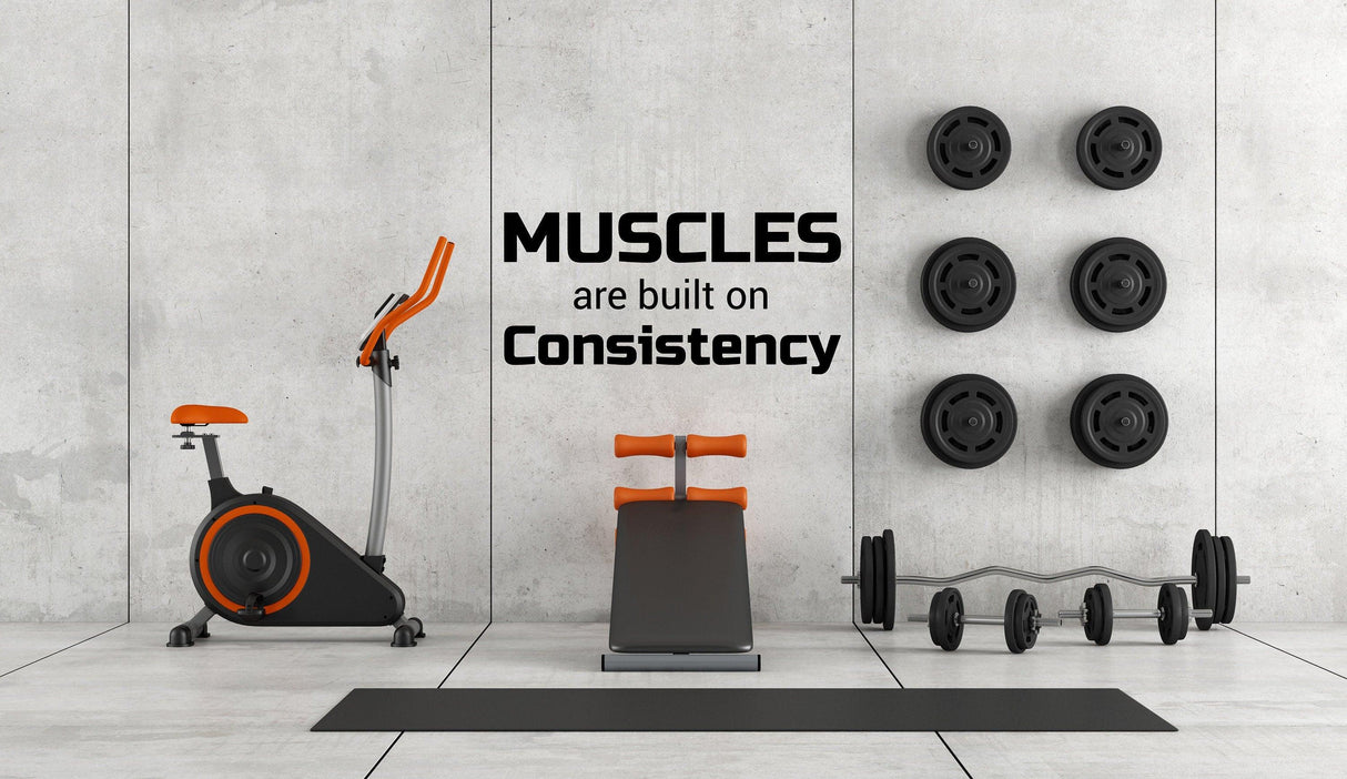 Gym interior featuring exercise bike, weights, and motivational wall decal about muscle building and consistency.