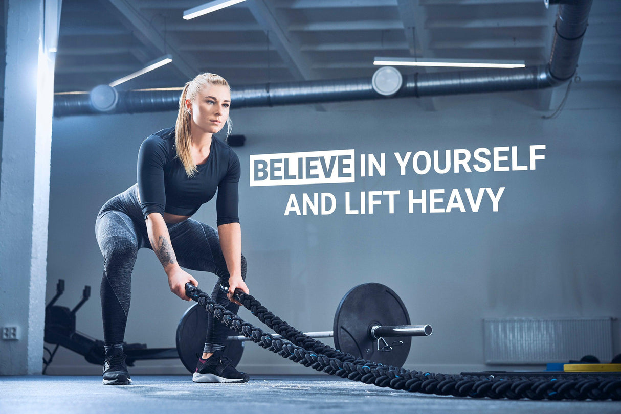 Motivational gym wall decal with the quote 'Believe in Yourself and Lift Heavy' in a modern fitness space.