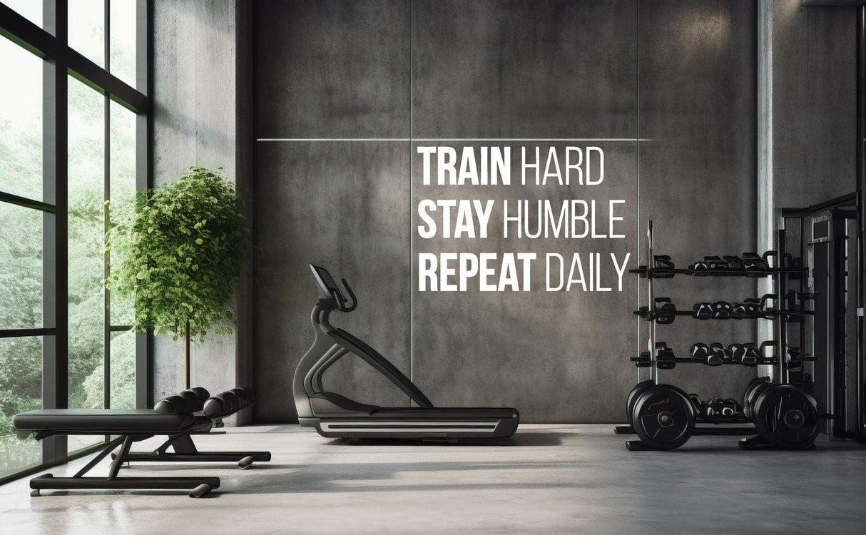 Gym with motivational wall decal: 'Train Hard, Stay Humble, Repeat Daily.' Inspiring workout environment.