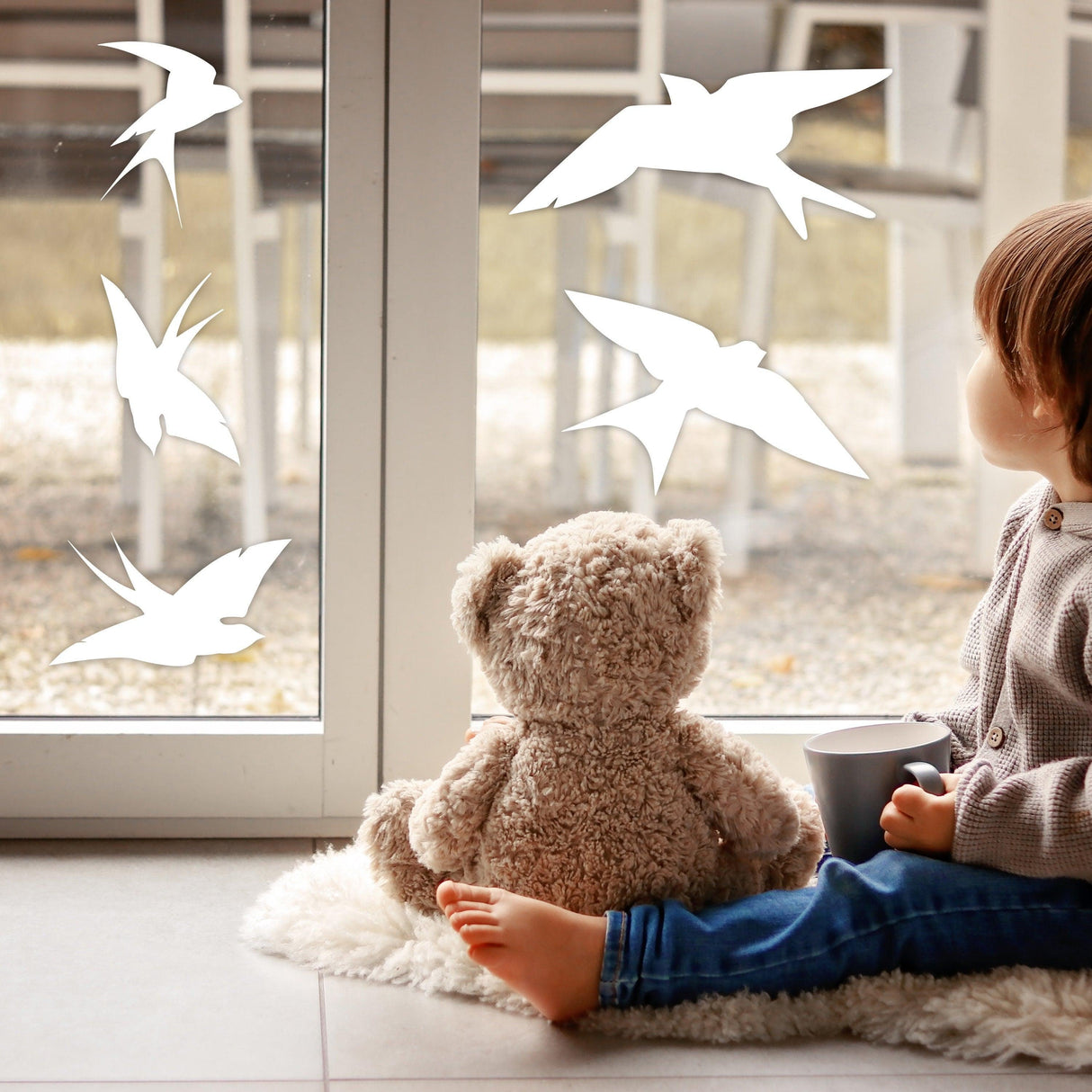 Child sitting by a window with anti-collision bird decals, promoting bird safety against window strikes.