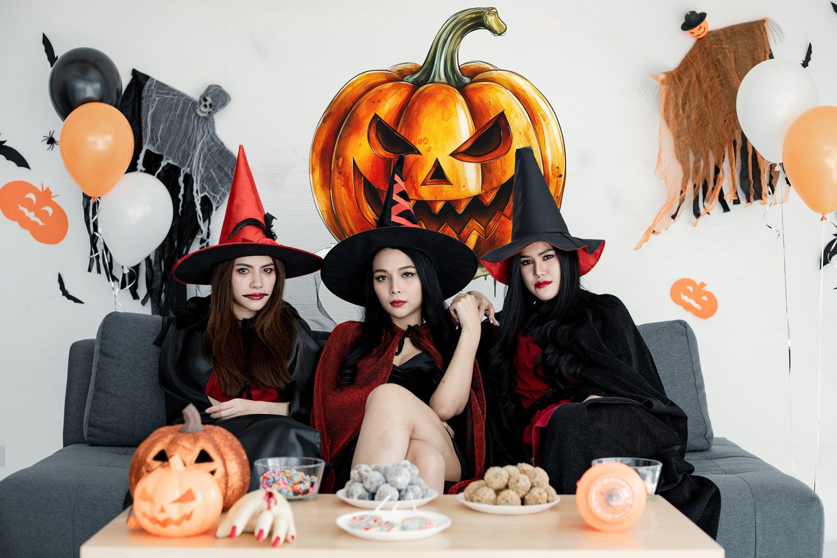Three women in witch costumes with Halloween decorations, including a laughing pumpkin and spooky treats.