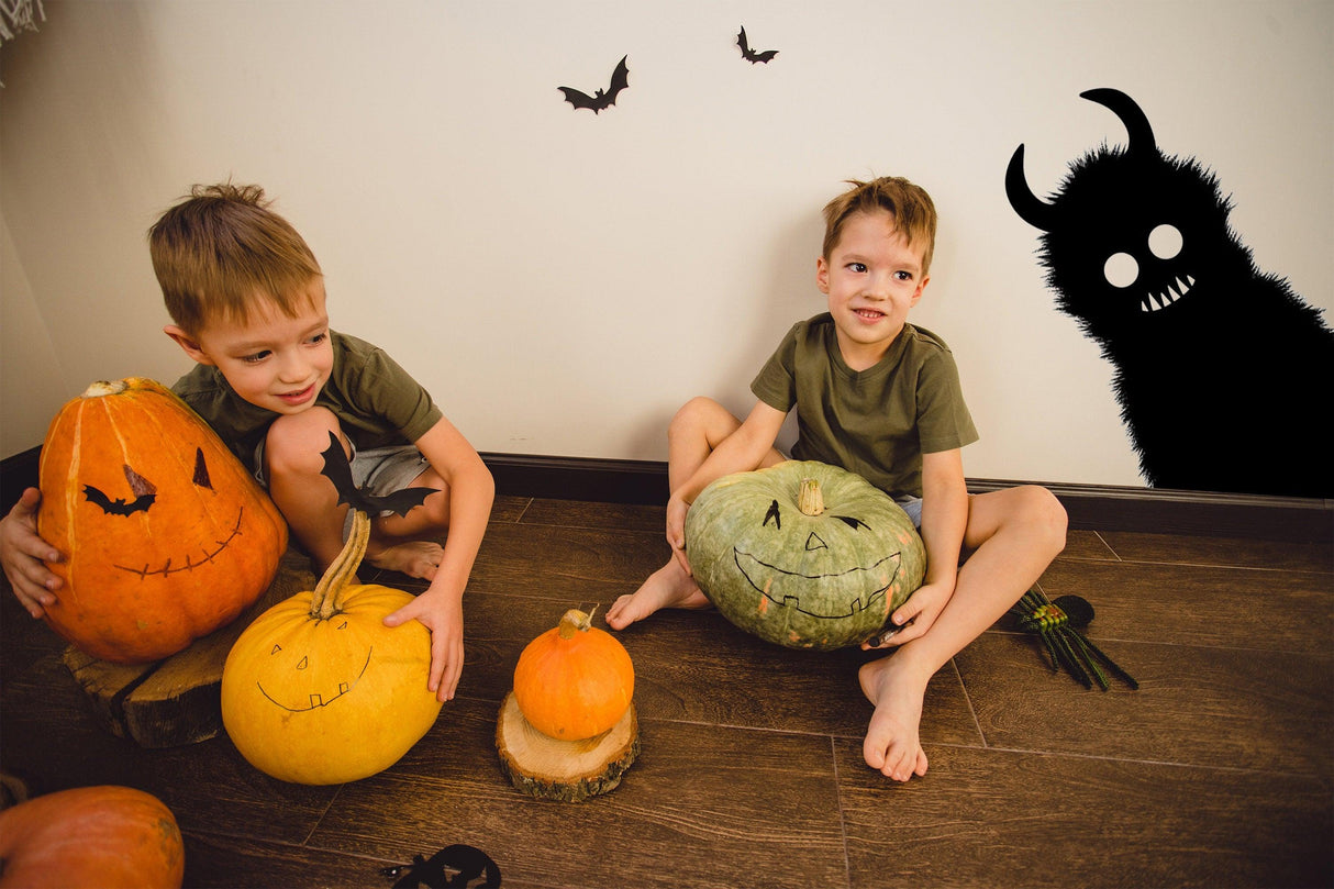 Two boys sitting with Halloween pumpkins, featuring a spooky monster shadow on the wall for a festive atmosphere.