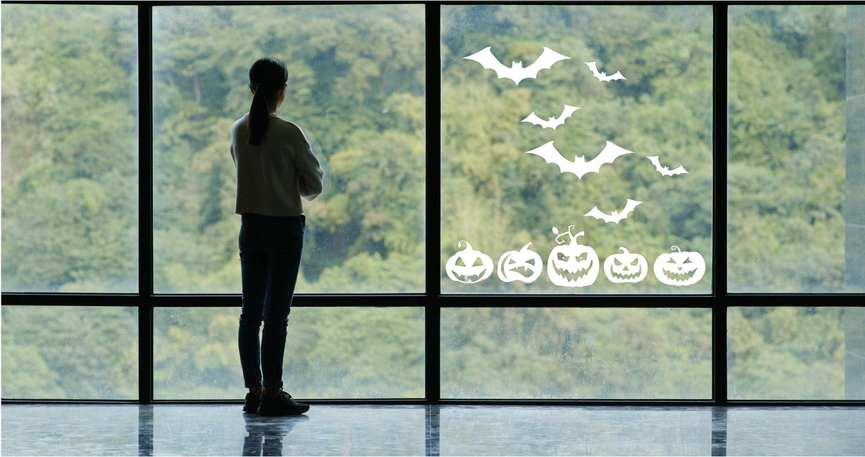 Woman admiring Halloween window decals of bats and pumpkins for festive decor.