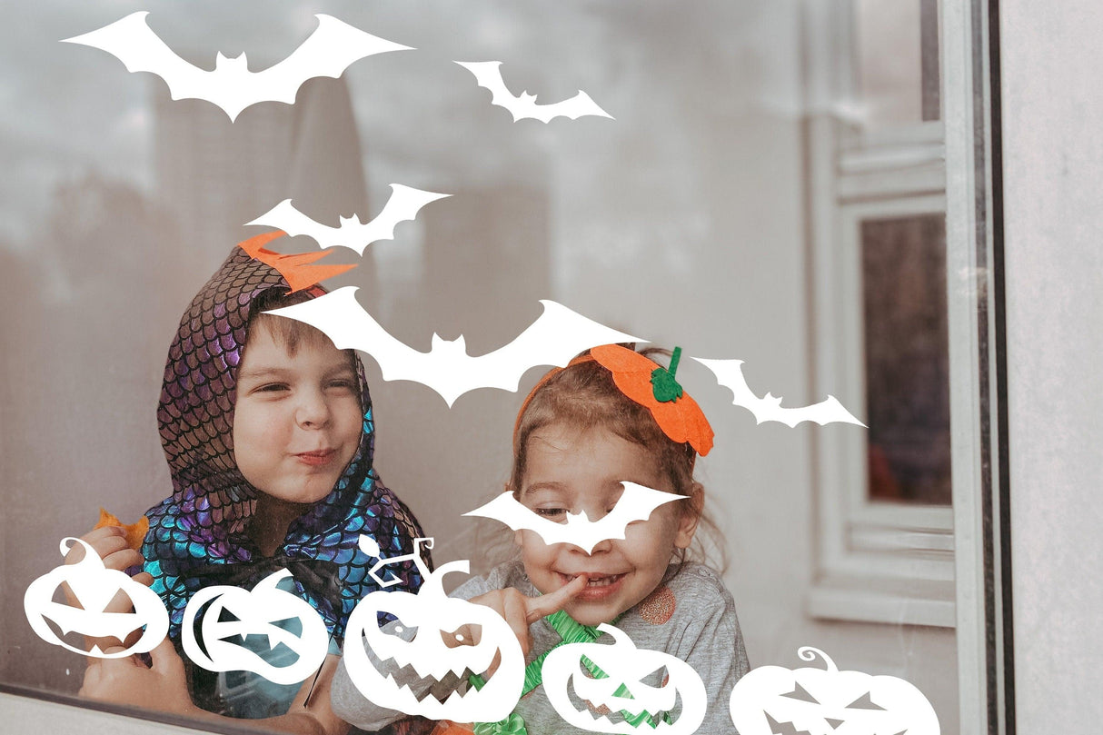 Kids in Halloween costumes enjoying spooky window decals of bats and pumpkins.
