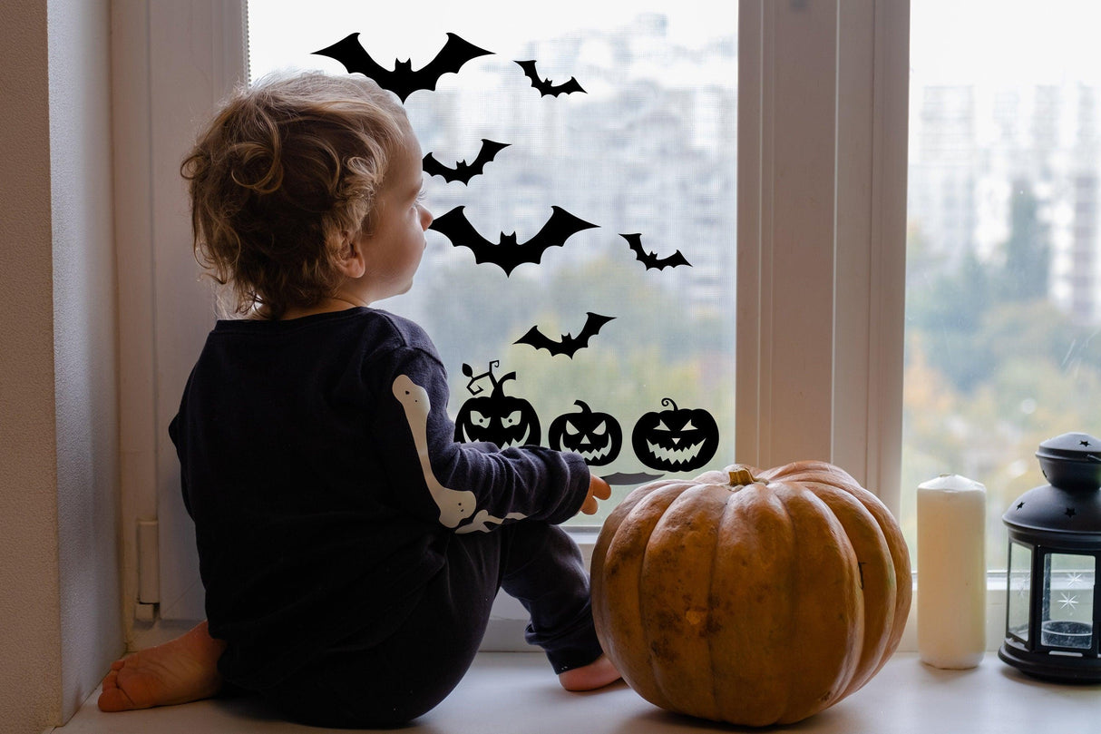 Child sitting by a window with Halloween window decals of bats and pumpkins, creating a festive spooky atmosphere.
