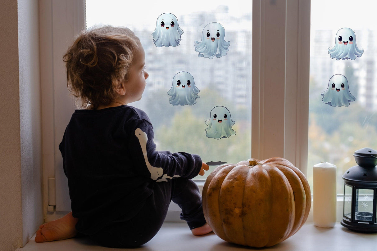 Child sitting by window with frosted ghost stickers, a pumpkin, and candle for Halloween decoration.