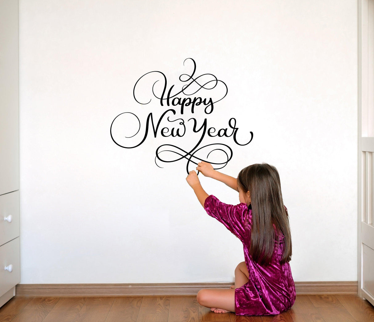 Girl applying a 'Happy New Year' vinyl sticker on a wall, enhancing festive home decor.