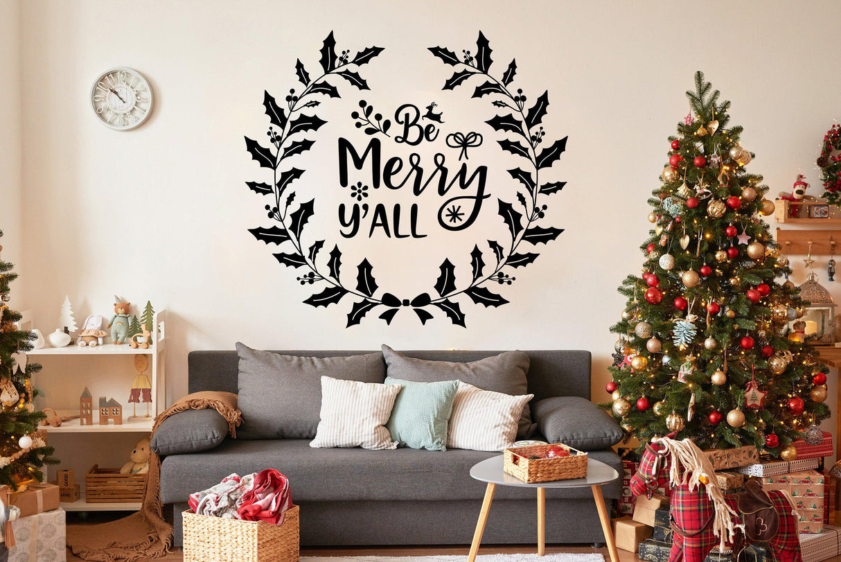 Charming wall vinyl sticker saying 'Be Merry y'all' above a cozy sofa in a festive living room with Christmas trees.