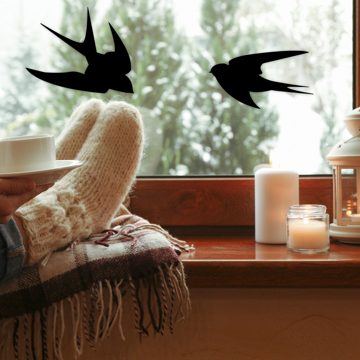 Cozy window scene featuring black bird deterrent decals and a person enjoying a cup of tea.