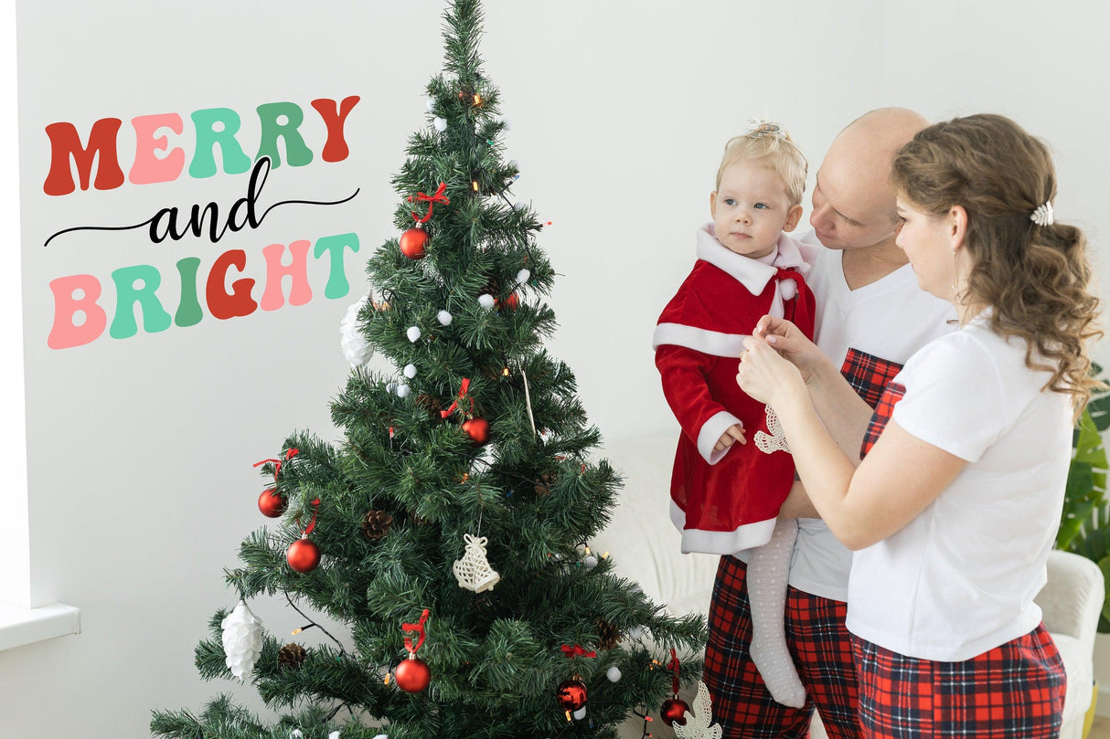 Family decorating a Christmas tree with "Merry and Bright" wall decal for a festive holiday atmosphere.