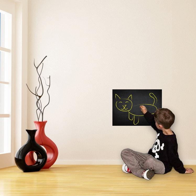 Child drawing a cat on a chalkboard decal in a modern living room with vases.