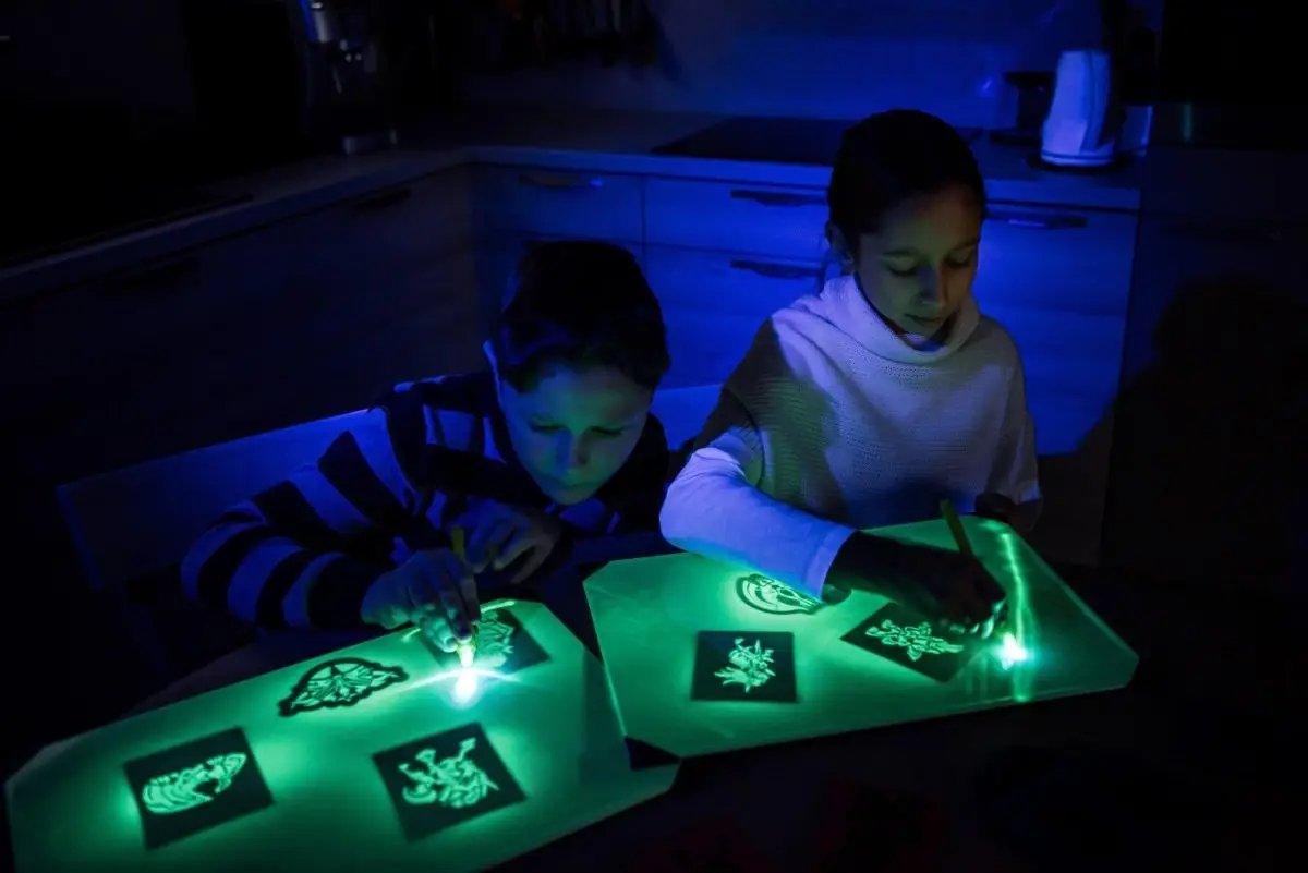 Kids using a light drawing board to create glowing art in a dark room, showcasing creativity and imagination.