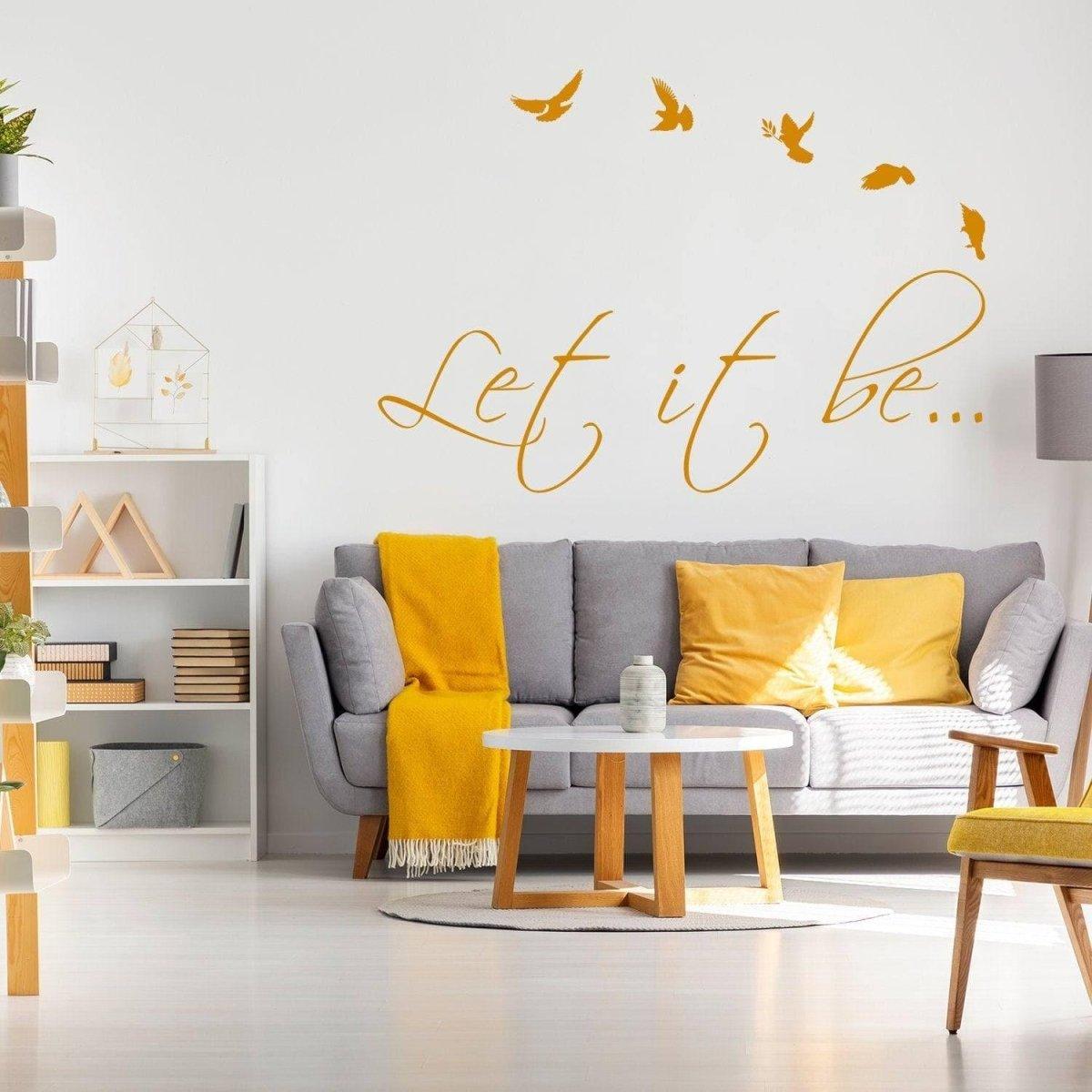 Motivational Harmony vinyl wall sticker 'Let it be' above a cozy living room couch with yellow accents and birds.