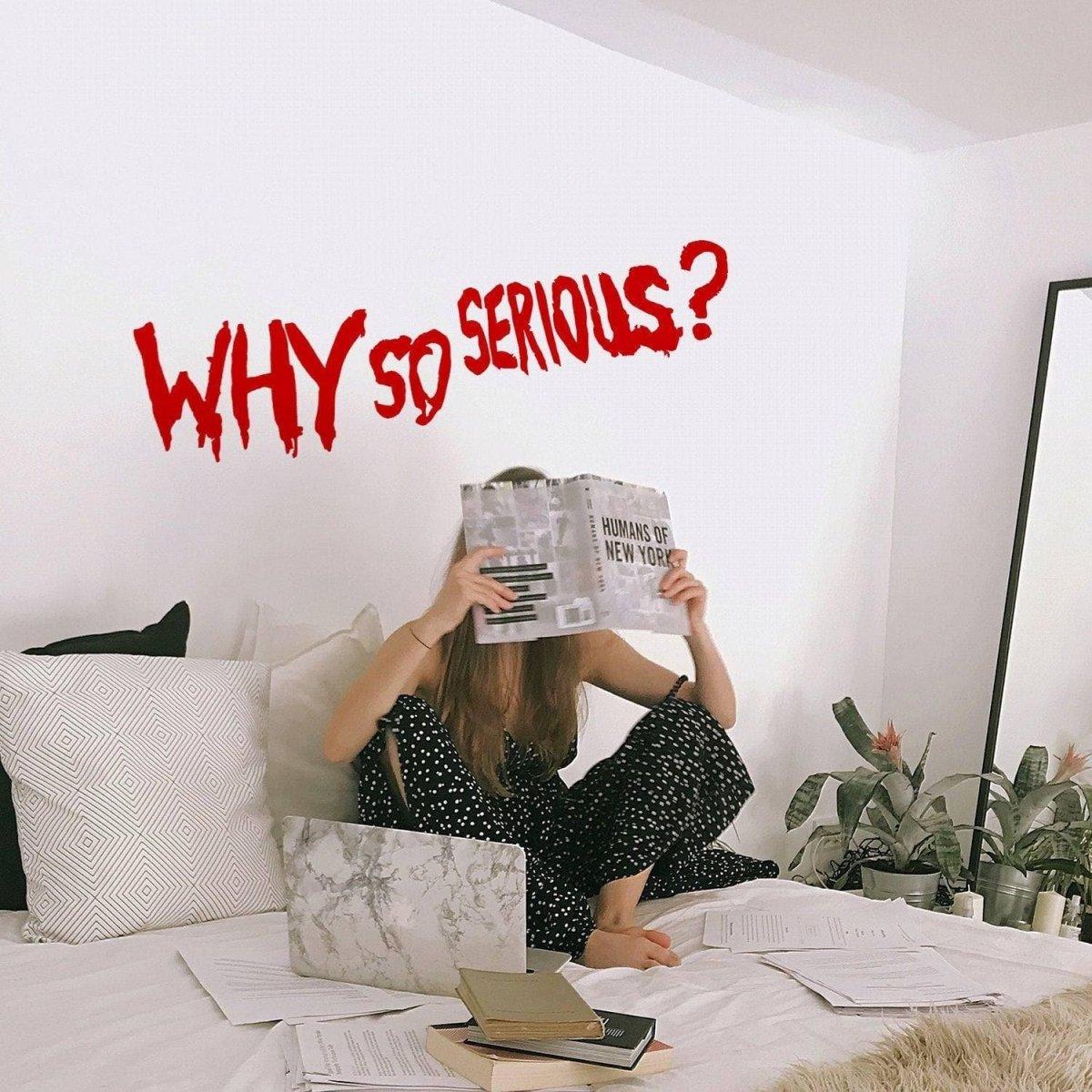 Young woman sitting on bed reading with 'WHY SO SERIOUS?' vinyl wall decal in a cozy interior setting.