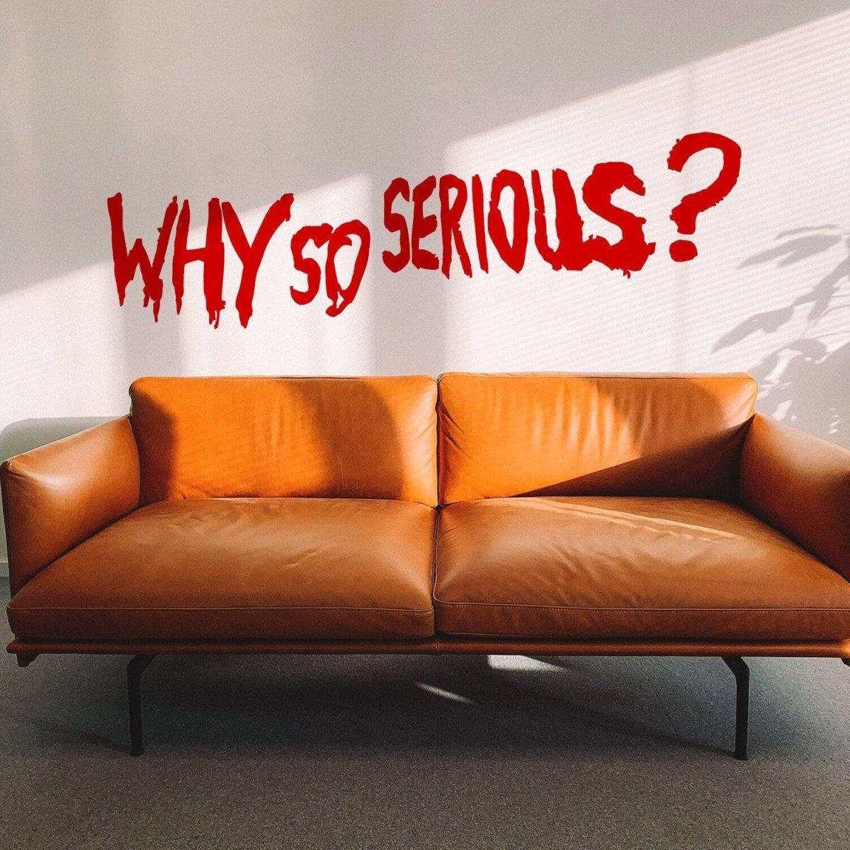 Joker-themed vinyl wall decal 'Why So Serious?' above a stylish brown leather sofa in a bright interior.