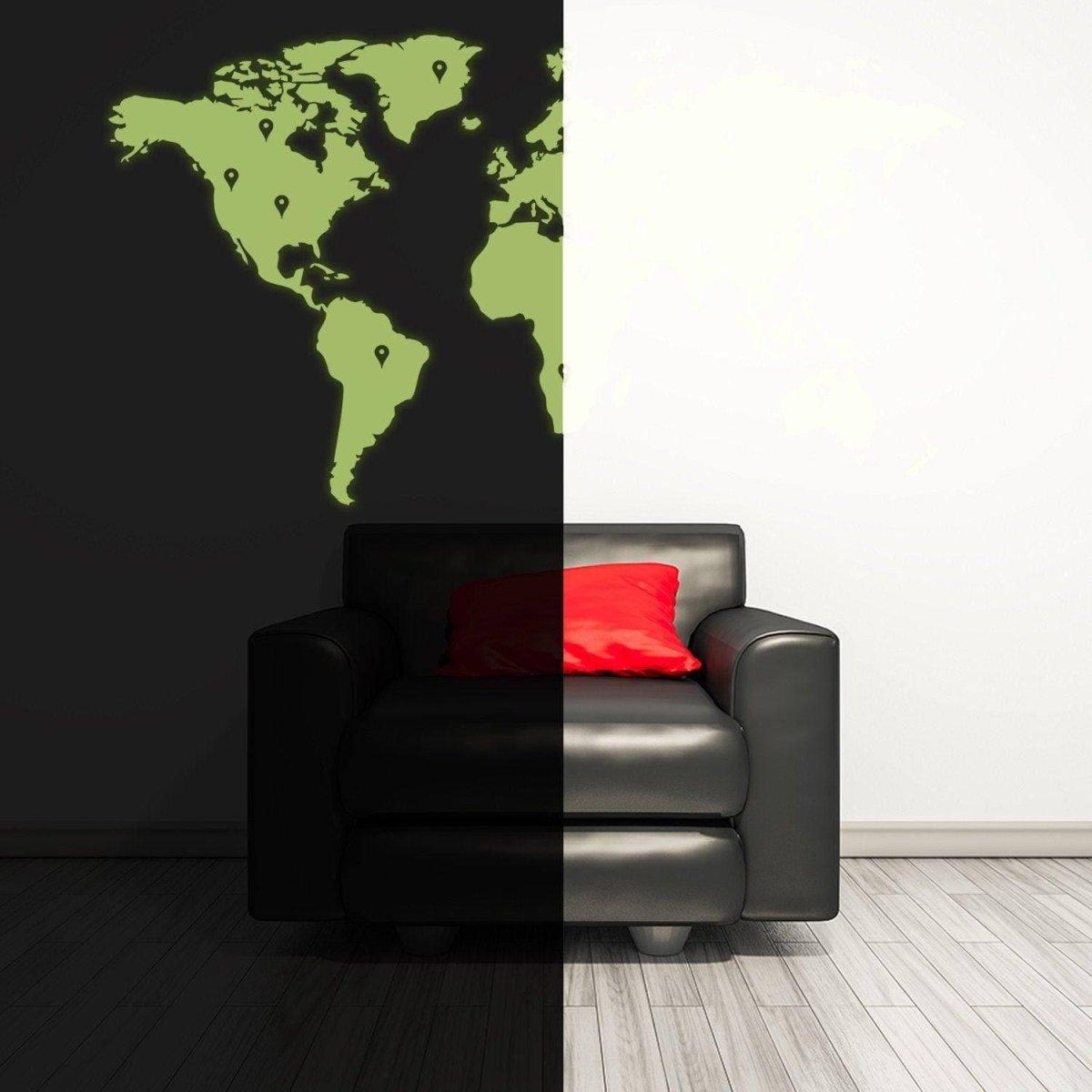 Glowing world map wall sticker illuminating dark room beside black chair with red pillow