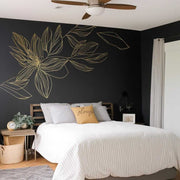 Elegant gold flower wall decal on dark wall above a minimalist bed in a stylish bedroom.