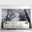 A dramatic misty forest wallpaper mural covers the entire living room wall, depicting tall, shadowy trees disappearing into fog. The grayscale tones create a moody, immersive atmosphere behind a modern beige sectional sofa and minimalist coffee table.