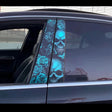 A close-up of a black car featuring two vivid vinyl decals on the B-pillars, showing a detailed blue skull and rose pattern with multiple skulls stacked vertically across both panels.