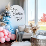 A party backdrop featuring a pastel balloon arch in pink, blue, and silver, with a white arch panel that has a custom black vinyl decal reading “Your Custom Text” in elegant script font.