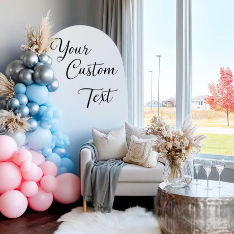 A party backdrop featuring a pastel balloon arch in pink, blue, and silver, with a white arch panel that has a custom black vinyl decal reading “Your Custom Text” in elegant script font.