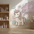A cozy children’s room with a large wall decal of a pastel cartoon unicorn beside a fluffy pink tree and surrounded by soft clouds and stars. The design features a sweet and whimsical aesthetic in shades of cream, pink, and mint, perfect for a girl’s nursery or bedroom.