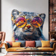 Colorful wall decal of a Pallas’s cat (manul) wearing large sunglasses with orange and purple reflections, printed in vivid detail and applied to a white indoor wall above a modern sofa with colorful cushions.