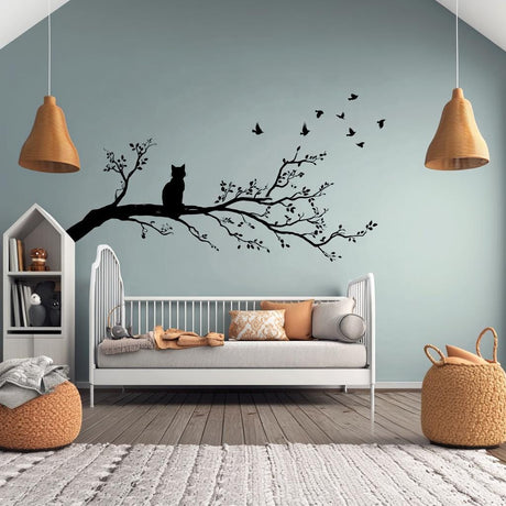 Vinyl wall decal of a cat sitting on a tree branch with flying birds, cut in solid black and applied to a pale green wall above a child&#39;s bed in a cozy, modern nursery.