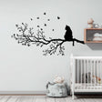 Vinyl wall decal of a cat sitting on a detailed tree branch with flying birds. The decal is solid black with no background and is applied above a crib in a soft-toned nursery.
