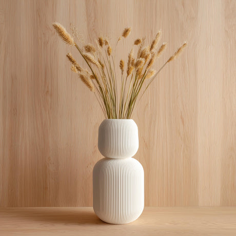 Tall 3D printed white geometric vase with ribbed texture, holding dried grass stems, displayed against a light wood background