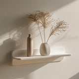 Minimalist 3D printed wall shelf in matte white, holding decorative vases and dried plants, mounted on a softly lit modern wall