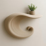 A beige 3D printed floating shelf in the shape of a curling wave, mounted on a light wall and holding a small potted plant on top.